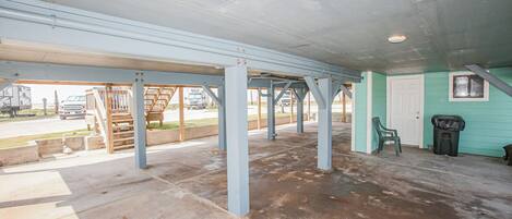 Un espace extérieur abrité, doté d’un sol en béton et de poutres métalliques, d’une porte et d’une poubelle.