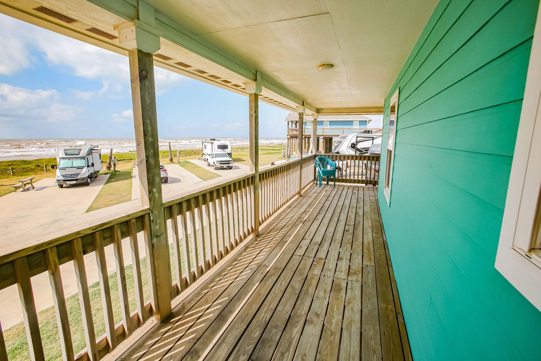 A covered porch with a view of the beach and RVs parked outside.
