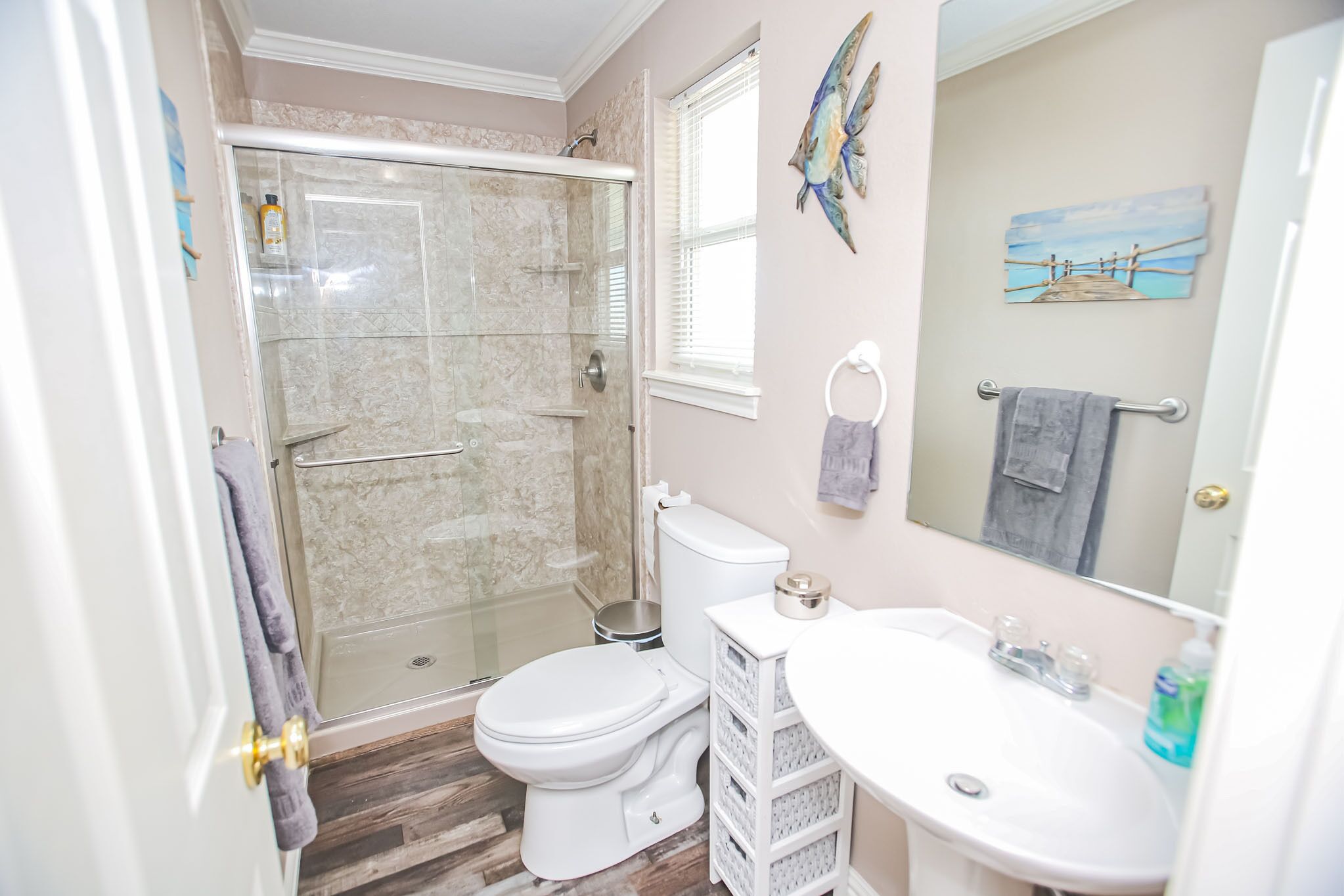 A bathroom with a glass shower enclosure, a toilet, a sink, and a mirror.