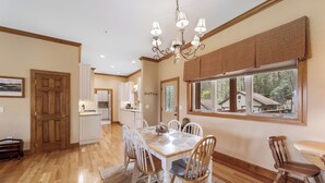 A dining area with a wooden table, white chairs, a chandelier, and a view of a house through a window. - Relaxed Retreat with Premiere Location and Views, Only 6 Steps to Get In, Garage (Whittier)