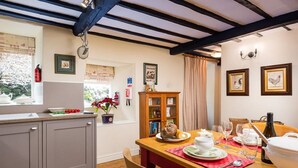 Una cocina acogedora con una mesa de madera lista para comer, una ventana con vistas y una estantería con libros y objetos decorativos.