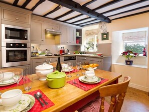 A modern kitchen with built-in appliances, a dining table set for four, and a window with a view of greenery. - Stone Beck (Ambleside)