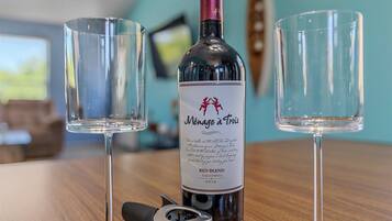 A bottle of wine with a label, two empty wine glasses, and a corkscrew on a wooden table.