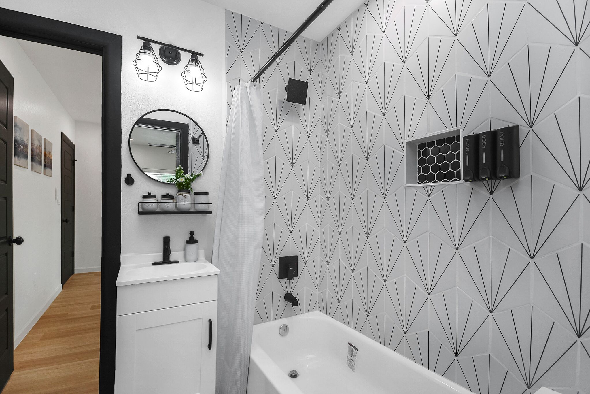 A modern bathroom with a white sink, a large mirror, and a geometric-patterned wall.