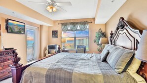 Ein Schlafzimmer mit einem großen Bett, einem Deckenventilator, Blick auf den Strand und einem Fenster mit Vorhängen.