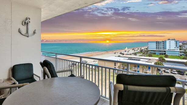 Ein Balkon mit Blick auf einen Sonnenuntergang über dem Meer, ein Stuhl und ein Tisch.