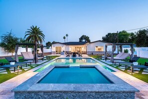 A rectangular swimming pool with lounge chairs and umbrellas, surrounded by a well-maintained lawn and a house in the background. - Resort Backyard @ The Arcadia Oasis! Tons of games (Phoenix)