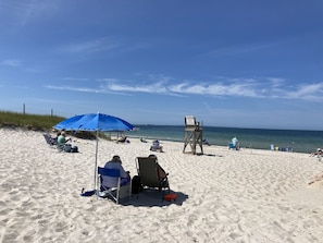 A sandy beach with several beach chairs and umbrellas, a lifeguard stand, and a clear view of the ocean.