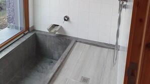Een badkamer met witte betegelde wanden, een douche met handdouche en een raam met houten kader.