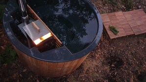 Een hottub met een houten constructie en metalen frame, omgeven door een houten terras en een kleine tuin.