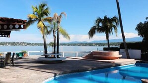A swimming pool with a view of a body of water and mountains, surrounded by palm trees and outdoor seating. - Incredibly Beautiful Big Villa For Up To 32 Guests (Tequesquitengo)