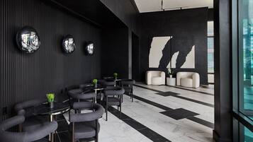 Un intérieur moderne avec des carreaux noirs et blancs au sol, des tables rondes entourées de chaises et une grande fenêtre donnant sur un immeuble.