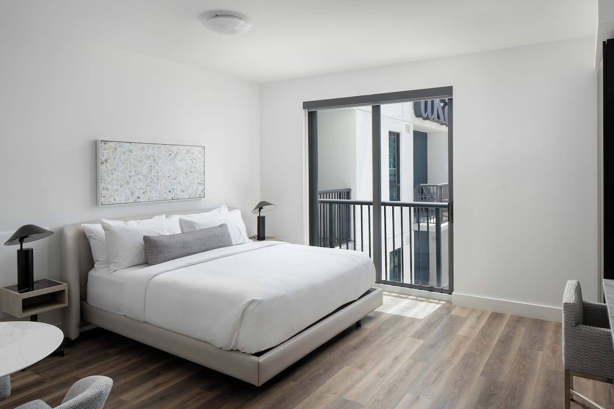Een moderne slaapkamer met een bed, nachtkastjes, een stoel en een grote glazen schuifdeur die leidt naar een balkon.
