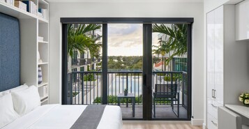 Habitación de hotel moderna con balcón, cama, estantería y vista a la ciudad.