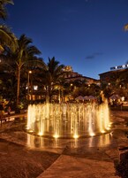 A nighttime fountain in a courtyard with palm trees and a building with illuminated signage.