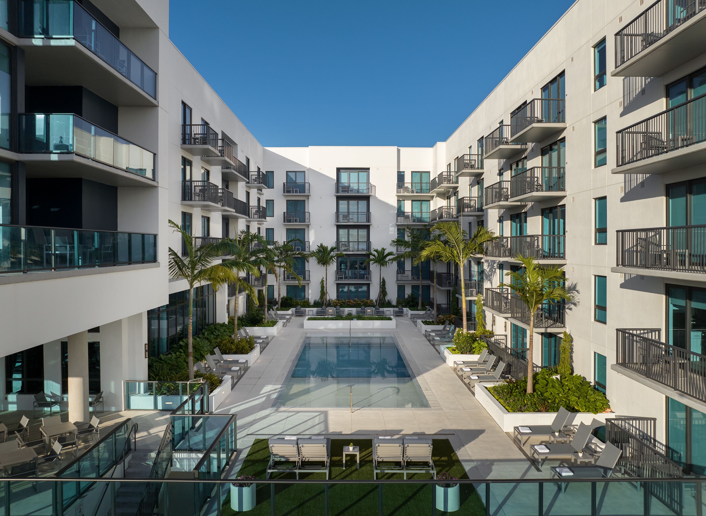 A modern hotel with a central swimming pool, multiple balconies, and outdoor seating areas.