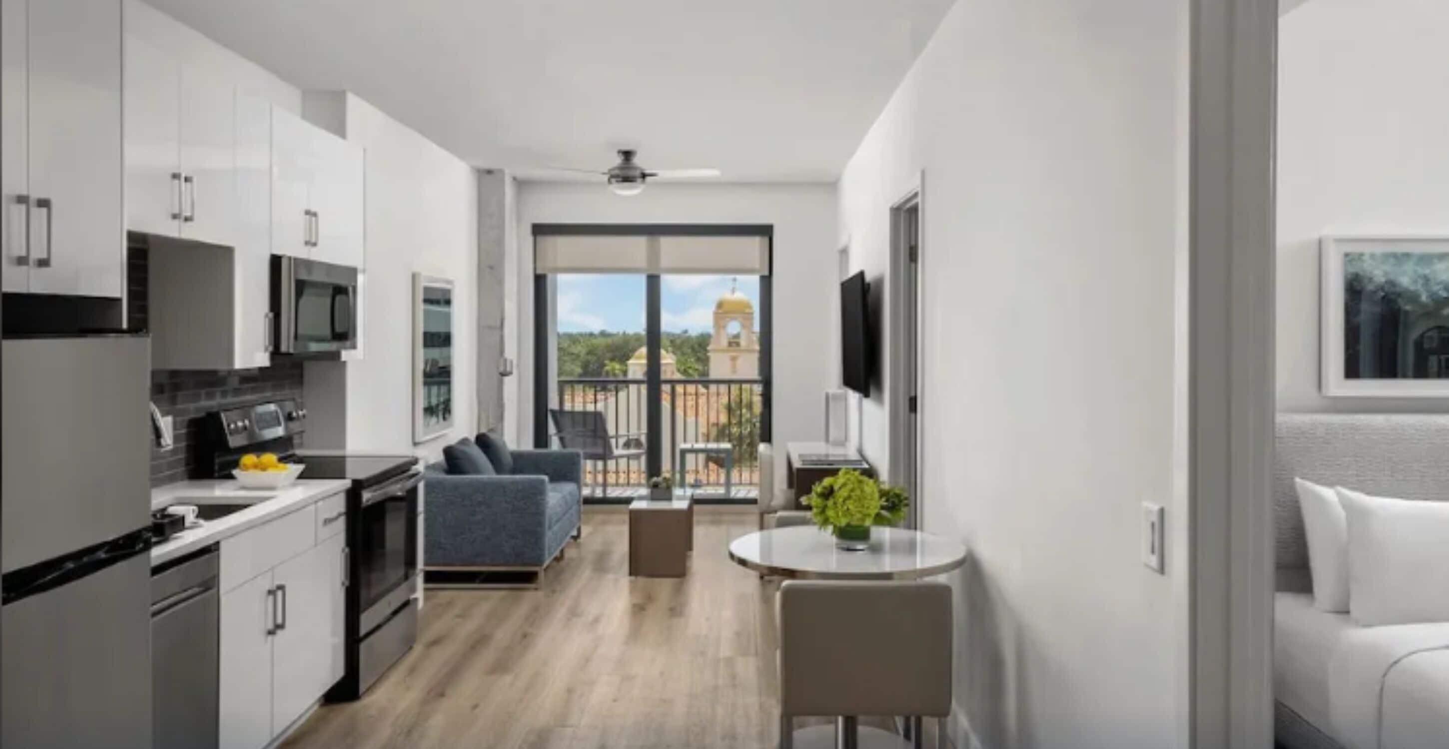 Un appartement moderne doté d’une cuisine, d’un coin repas et d’un balcon offrant une vue sur un immeuble.