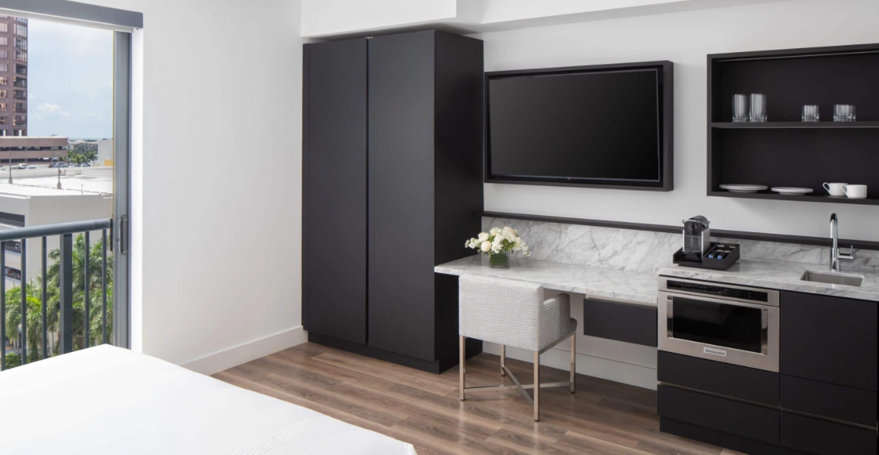 A modern kitchen with a marble countertop, a built-in oven, and a black TV mounted on the wall.