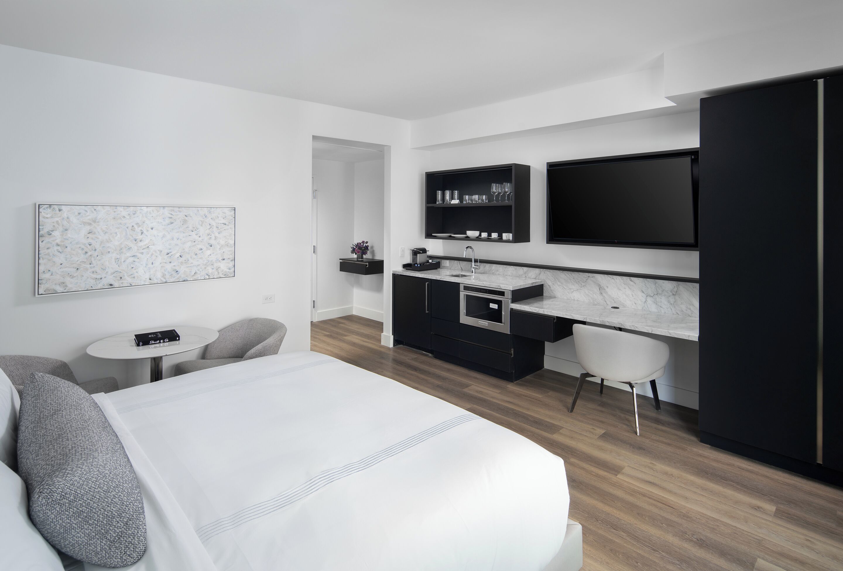 A modern hotel room with a large bed, a desk, a flat-screen TV, a small table, and a chair.