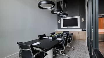 Une salle de conférence dotée d’une longue table, de chaises noires, d’un grand téléviseur à écran plat et d’un luminaire suspendu moderne.