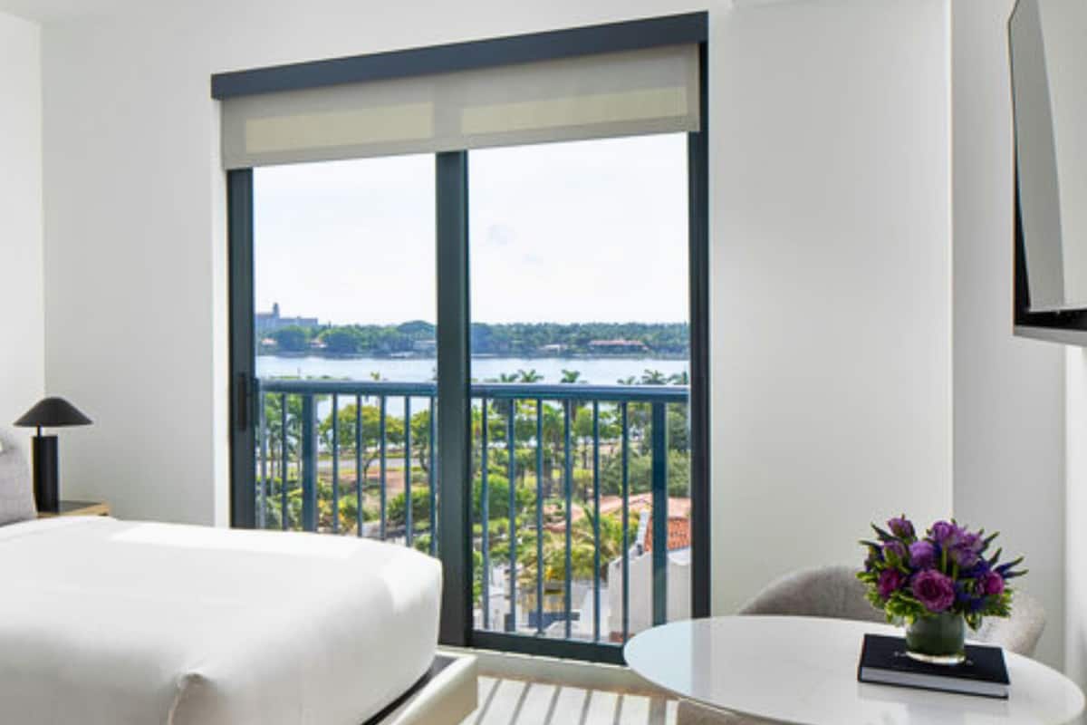Een hotelkamer met een groot bed, een klein tafeltje met een bloevas en een balkon met uitzicht op de stad.