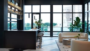 Eine moderne Bar mit Bartresen, Hockstühlen und Flaschenregalen. Große Fenster bieten Blick auf die Stadtlandschaft.