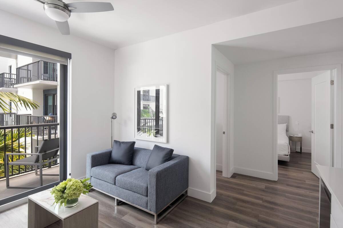 Een moderne woonkamer met een grijze bank, een bijzettafeltje met een bloevas, en een balkon met uitzicht op de omgeving.