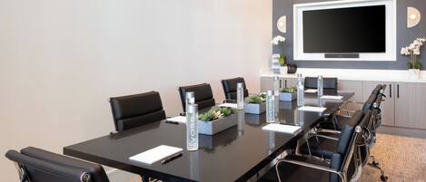 Una sala de conferencias con una mesa larga, sillas negras, un televisor de pantalla plana y luminarias modernas.