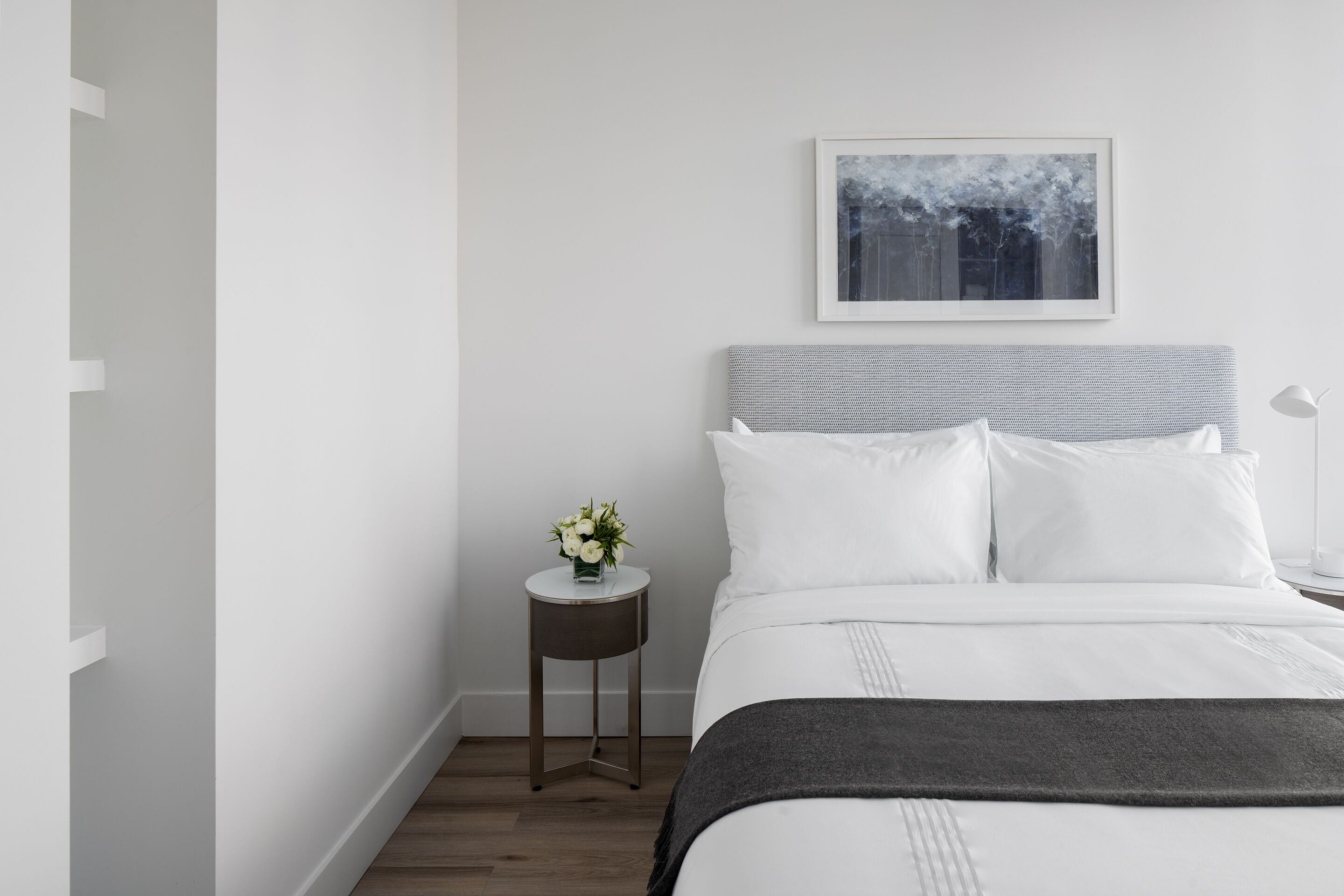 Una camera da letto dal design minimalista, con un letto, un comodino con un vaso di fiori e un quadro appeso alla parete.