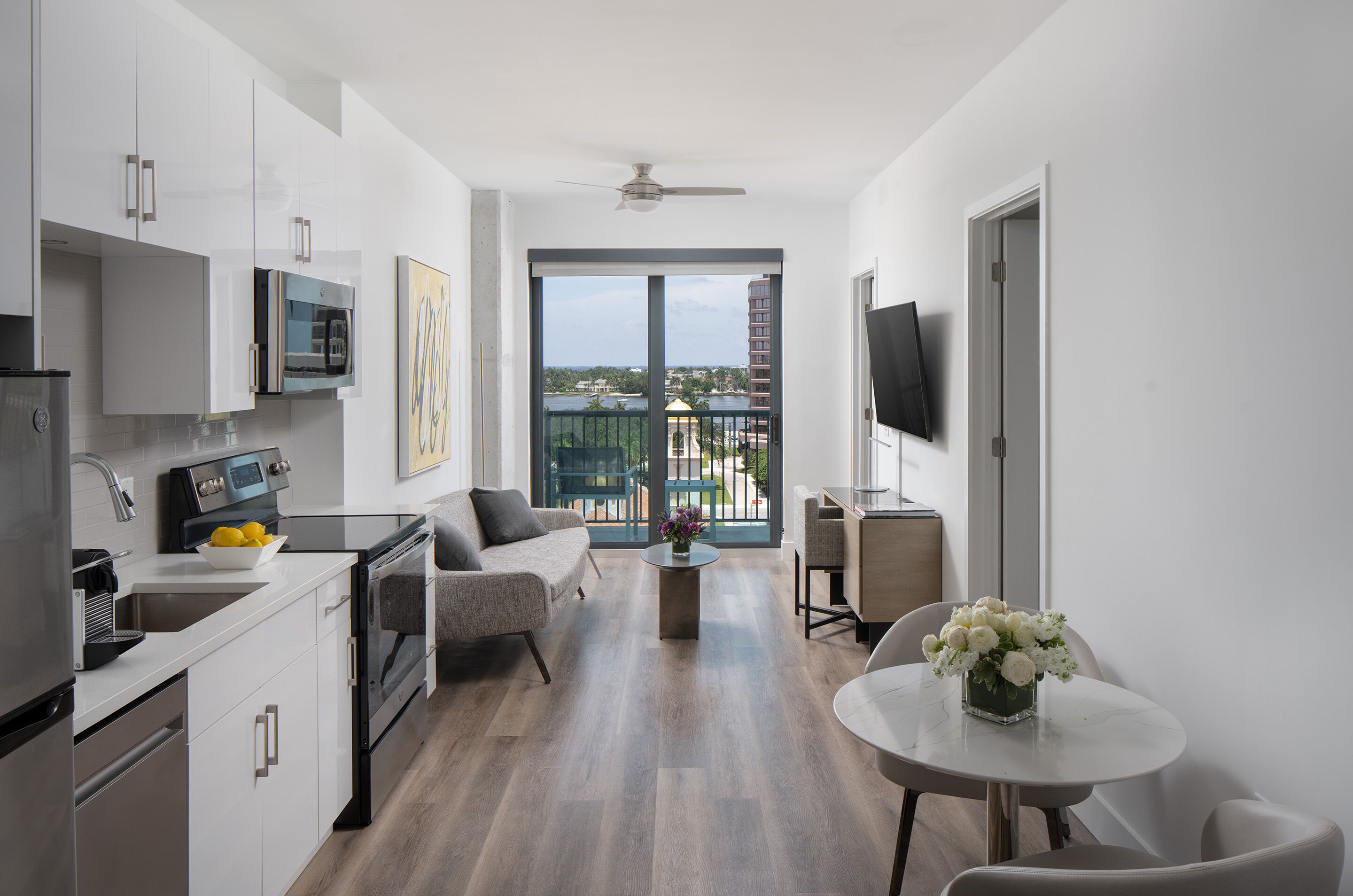 A modern kitchen with a dining area, a balcony with a view, and a flat-screen TV.