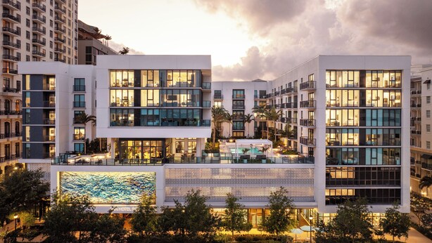 Ein modernes Hotel mit mehreren Etagen, großen Fenstern und einem Poolbereich.
