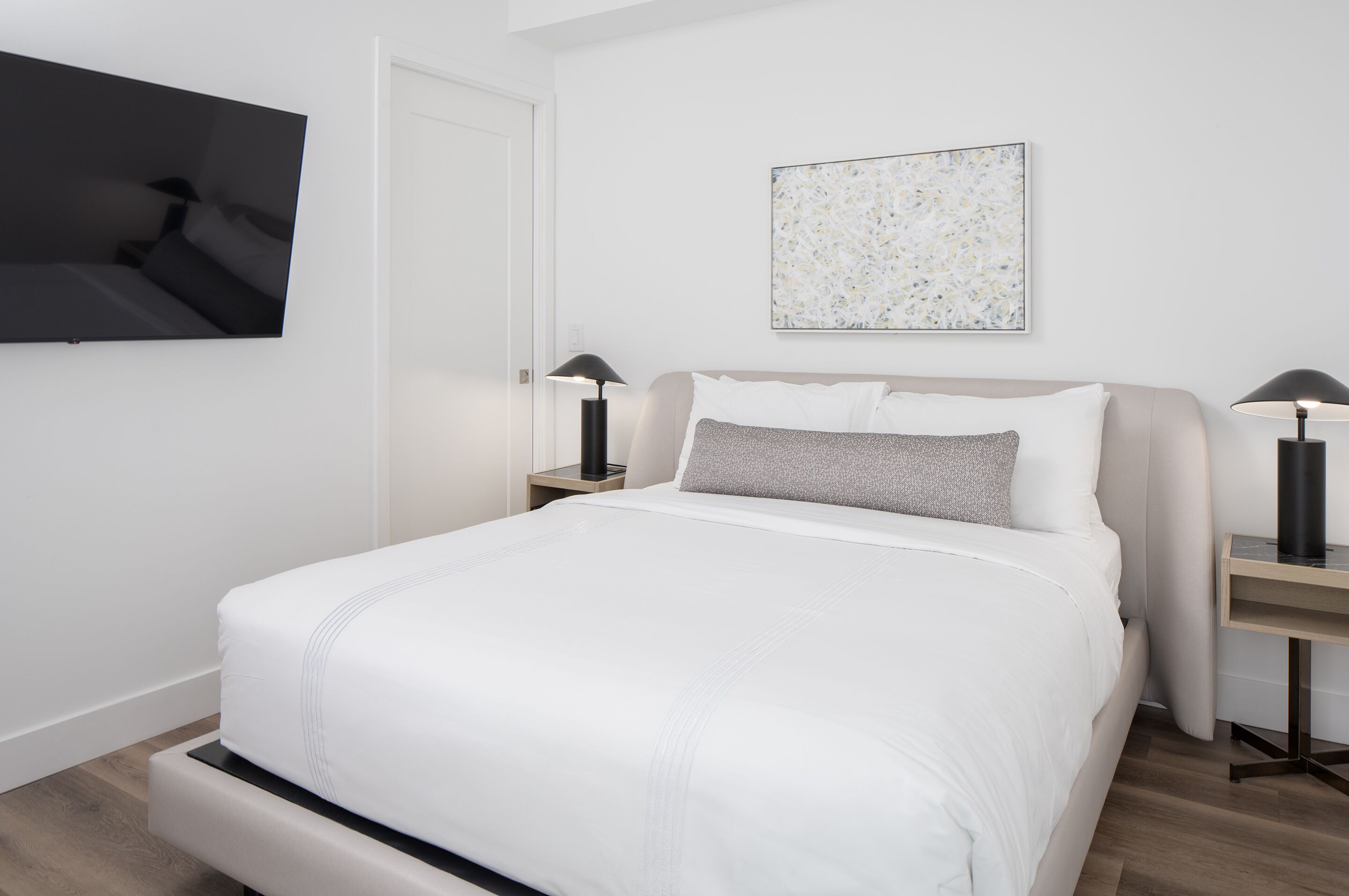 Ein modernes Schlafzimmer mit einem großen Bett, einem flachbildfernseher an der Wand und minimalistischer Einrichtung.