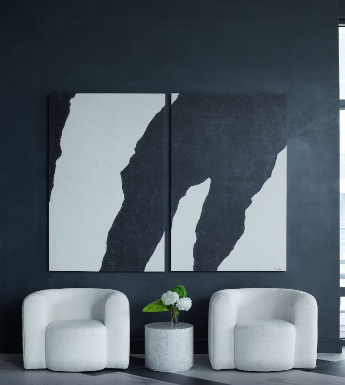 A modern room with two white armchairs, a small round table with a vase of flowers, and two large abstract paintings on the wall.