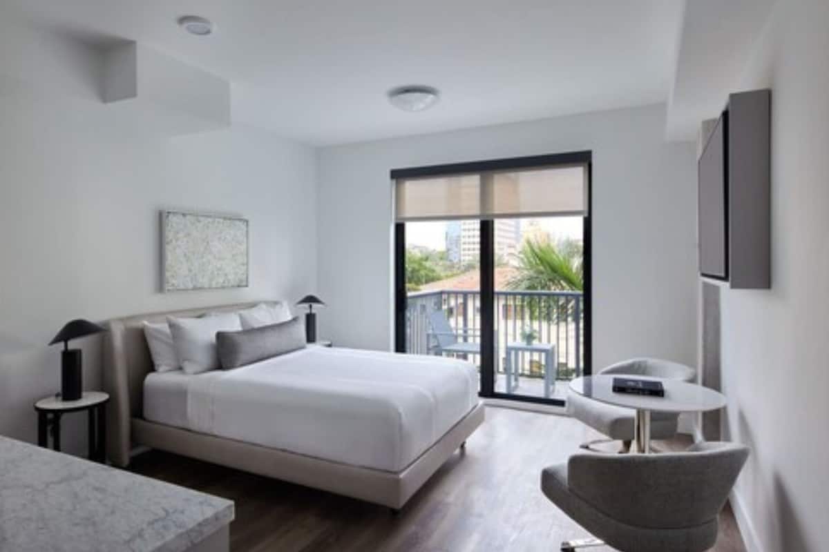 Een moderne hotelkamer met een bed, een tafeltje, een stoel en een balkon met tuinmeubilair.
