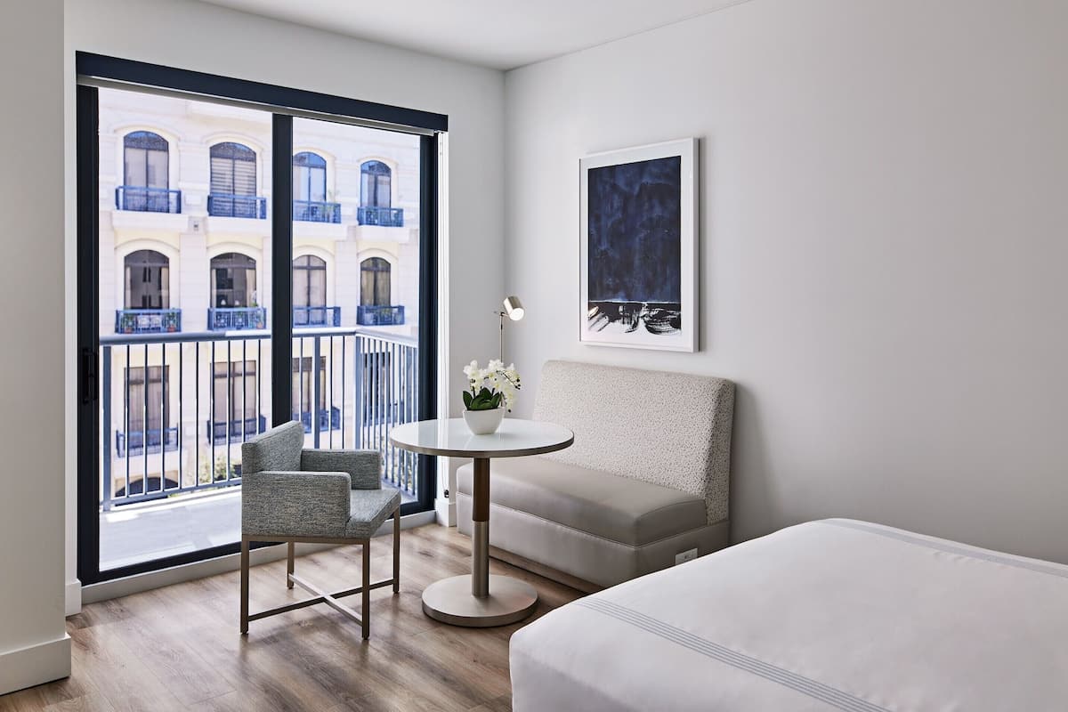 Een moderne hotelkamer met een groot raam, een ronde tafel met een bloemenvaas, een bank en een bed.