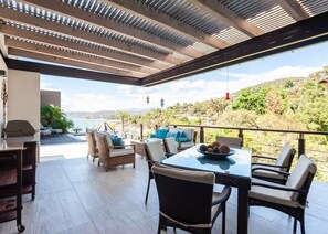 A patio with a table and chairs, a grill, and a view of the landscape.