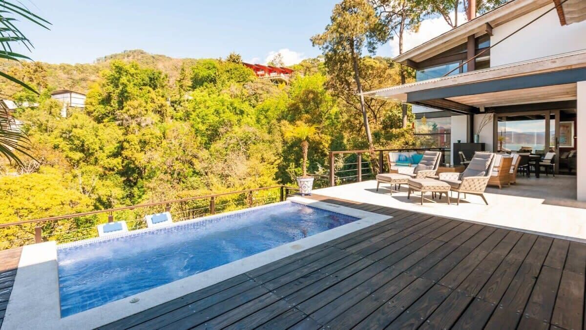 A modern house with a wooden deck, a swimming pool, and outdoor furniture.