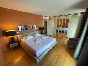 Quarto de hotel com uma cama grande, mesa de cabeceira com abajur, guarda-roupa e espelho.