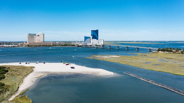 An aerial view of a coastal city with a prominent modern building, a bridge, and a sandy beach area.