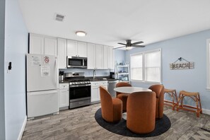 A modern kitchen with white cabinets, a stove, microwave, and a dining area with a round table and chairs.