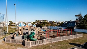 A playground with various play structures, including a slide and climbing frames, surrounded by a wooden fence.