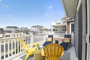 A balcony with yellow chairs and a table, overlooking a residential area with houses.