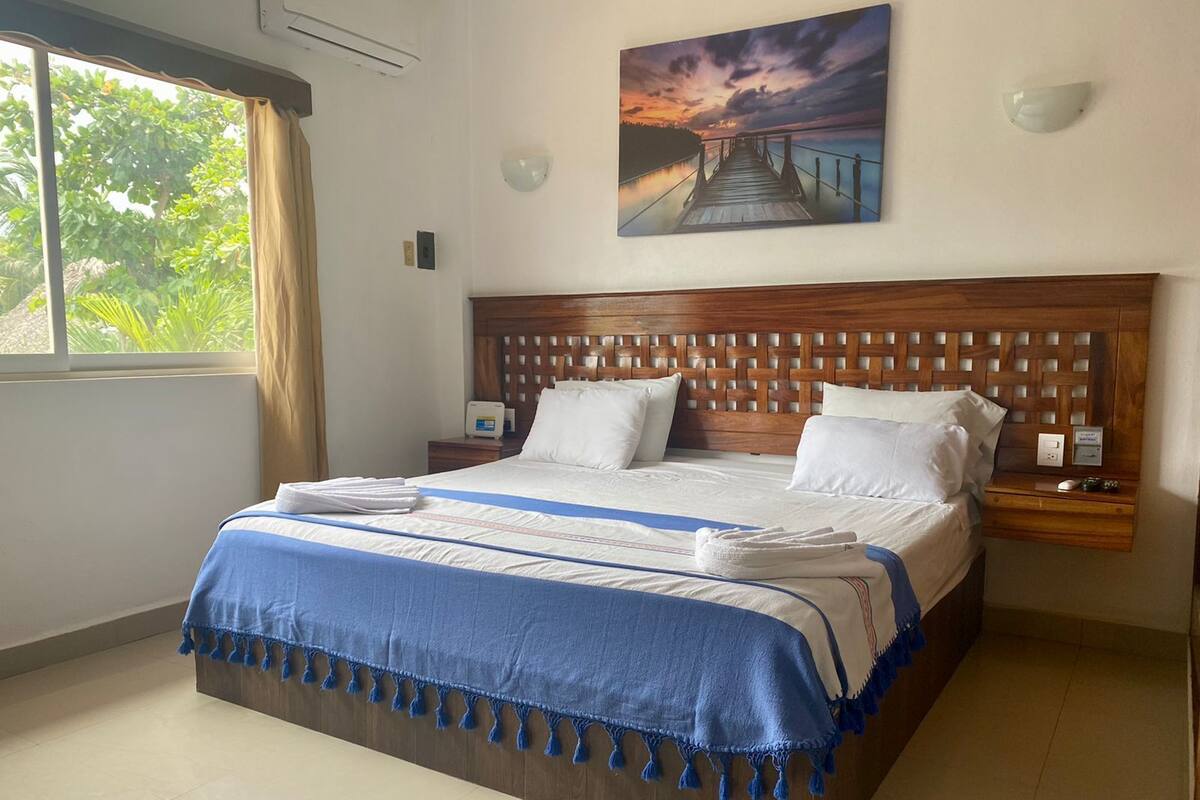 Una habitación de hotel con una cama grande, cabecera de madera y un cuadro de una puesta de sol sobre un muelle.