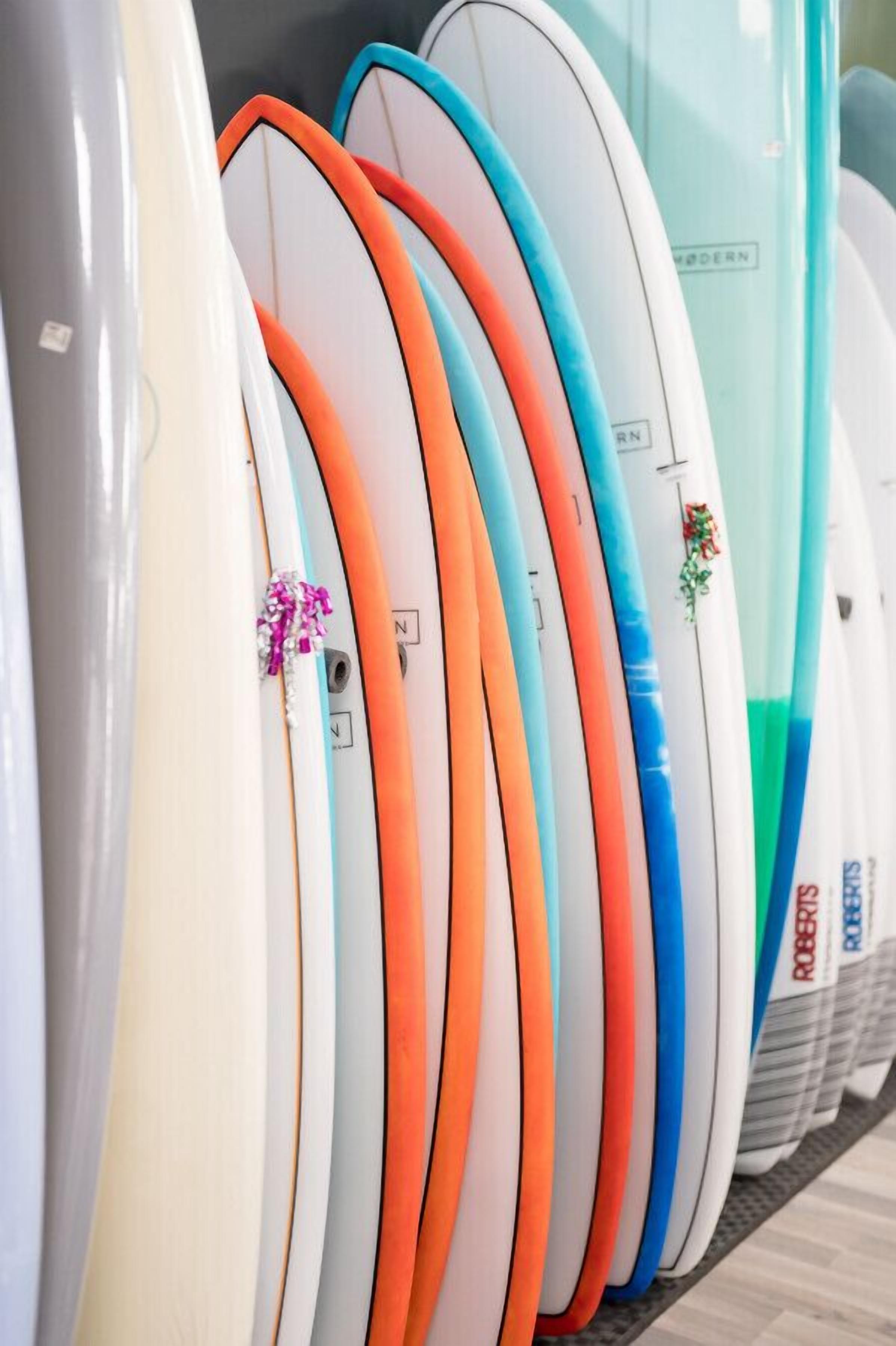 Eine Reihe von Surfbrettern in verschiedenen Farben und Designs, darunter ein weißes mit einem rosa Etikett und ein blaues mit einem grünen Design.