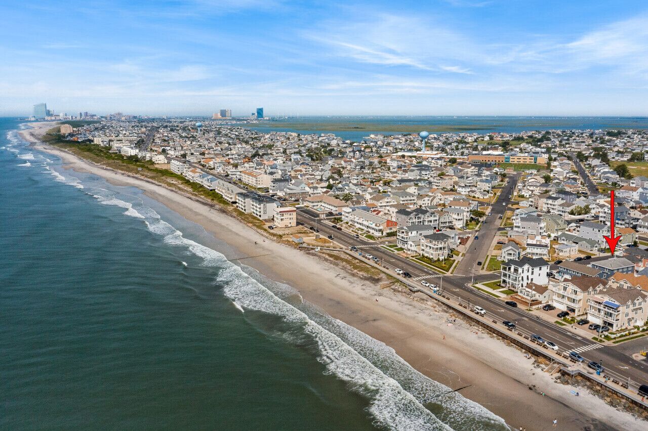 Une vue aérienne d’une ville côtière, avec une plage, des immeubles résidentiels et un bâtiment rouge imposant.