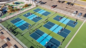 An outdoor tennis court complex with multiple courts and a parking area.