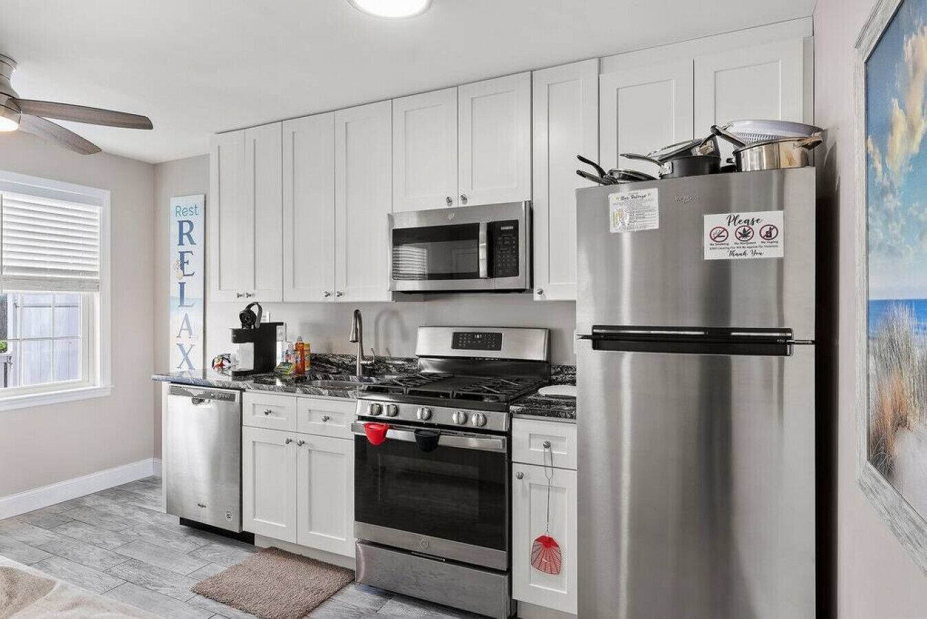 A modern kitchen with stainless steel appliances, white cabinetry, and a view of the outdoors through a window.