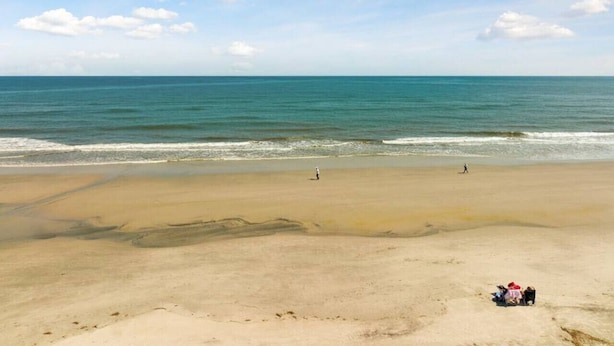 A beach with a clear sky, calm sea, and a few people walking.
