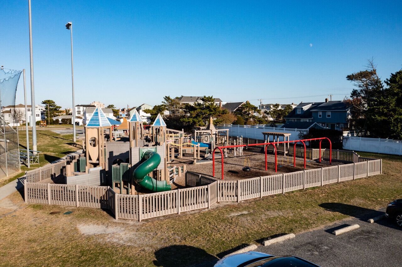 A playground with various play structures, including a slide and climbing frames, surrounded by a wooden fence.