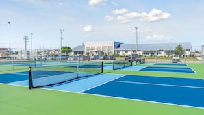 A tennis court with multiple courts, a net, and a building in the background.
